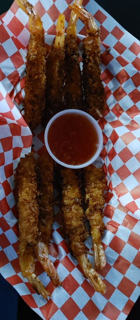Eight coconut-crusted prawns fried golden, fanned around a pot of sweet chilli sauce on red checked paper.