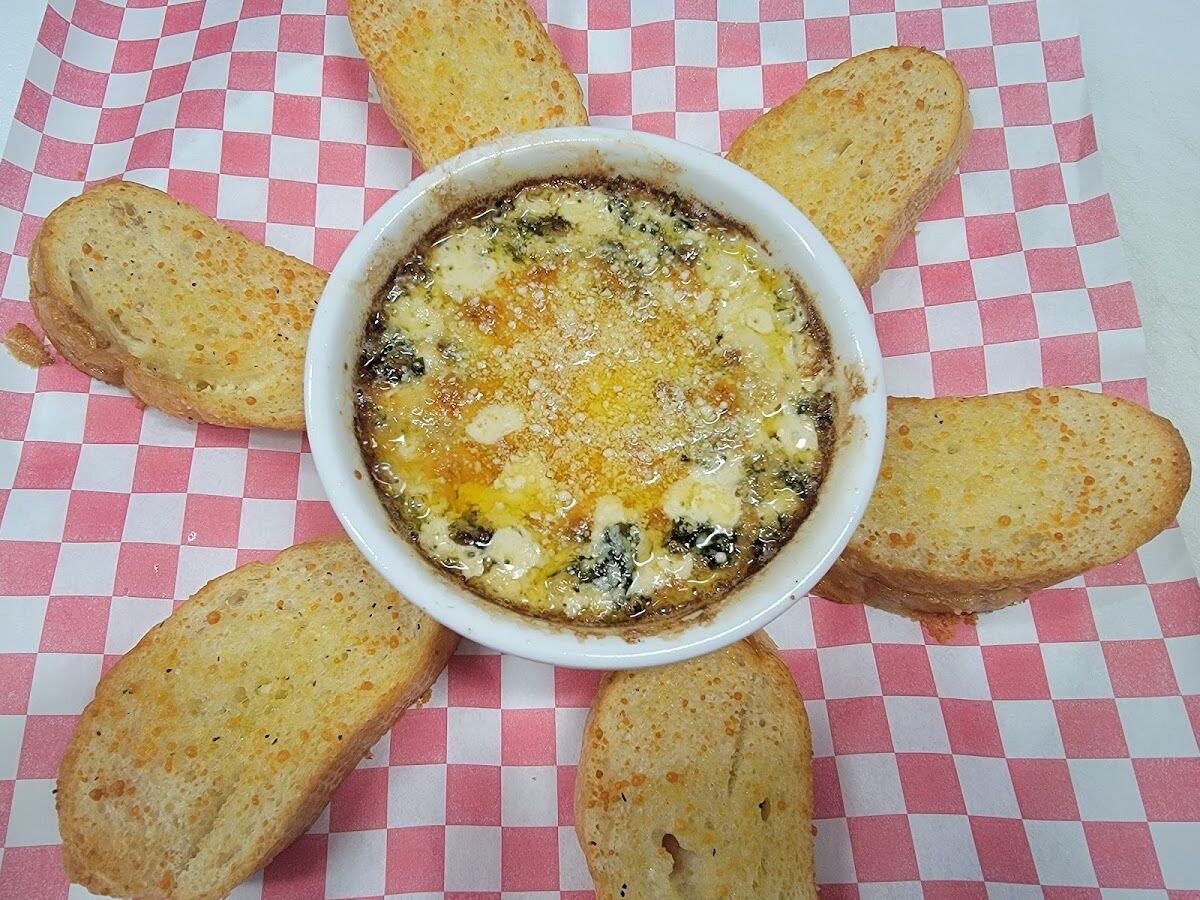 Baked spinach and artichoke dip, browned and bubbling under parmesan, ringed by six slices of toasted crostini.