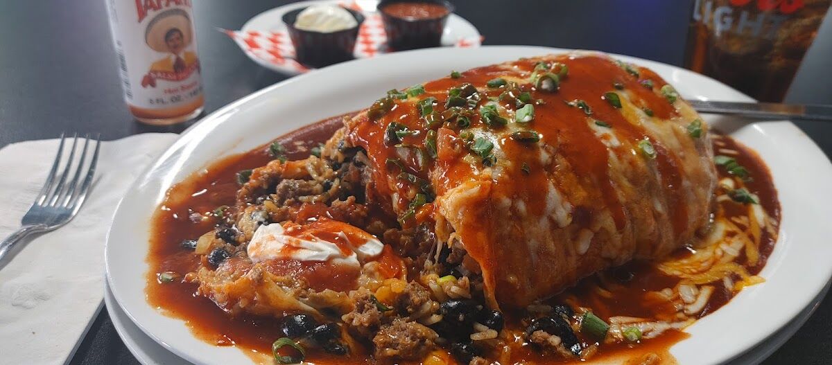 A wet burrito smothered in red sauce and melted cheese, cut open to show seasoned beef, black beans, rice and sour cream.